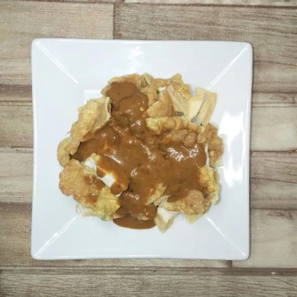 Gunting lontong, tahu dan telur di atas piring saji, siram dengan bumbu kacang.