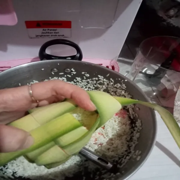 Lalu beri kapur sirih, aduk merata, isi cangkang ketupat dengan beras.
