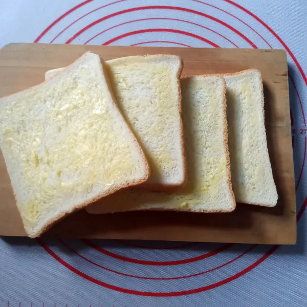 Oles tipis kedua permukaan roti tawar dengan butter.