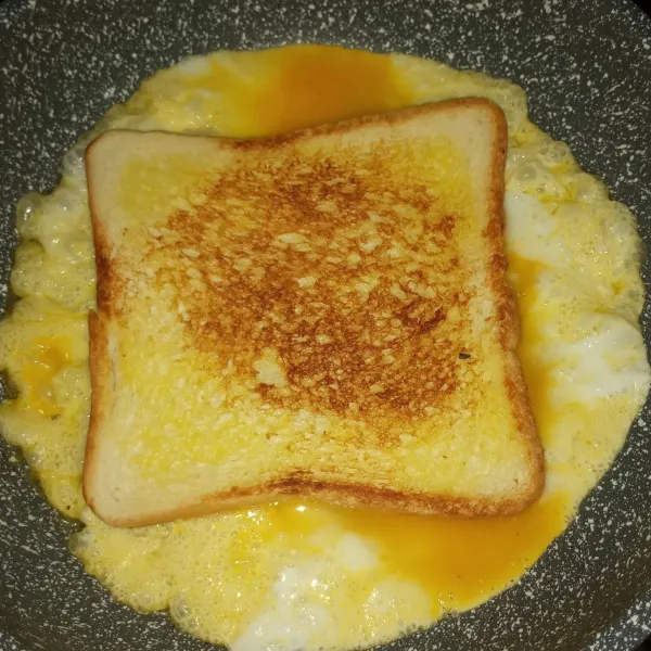 Kocok telur, bubuhi garam, dan lada. Beri sedikit butter d iwajan lalu tuang setengah bagian telur. Taruh selembar roti tawar panggang.