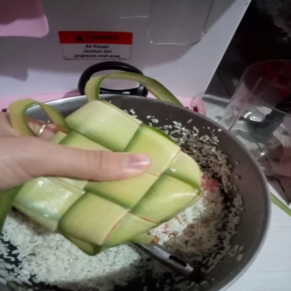 Isi cangkang ketupat dengan beras sampai terisi setengahnya.