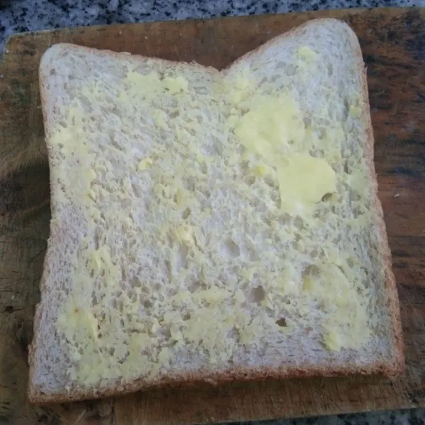 Olesi permukaan roti dengan margarin.