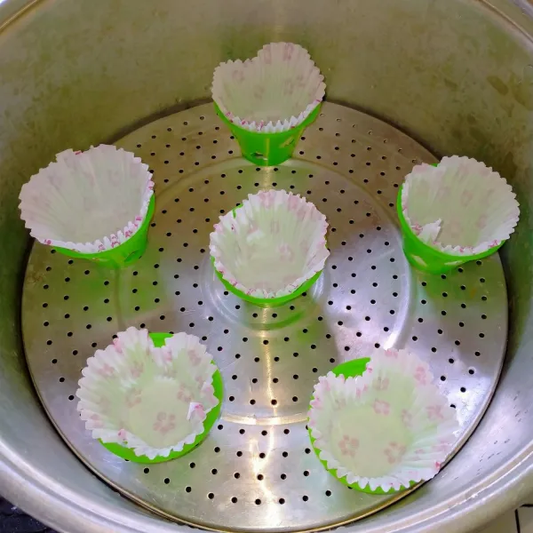 Panaskan panci pengukus dan juga cetakan didalamnya yang telah di beri 2 lembar kertas roti, tanpa mengoles minyak atau apapun. Gunakan api besar dan panci pengukus sampai beruap banyak.