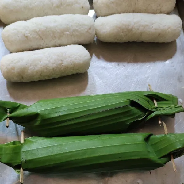 Siapkan daun pisang lalu ambil beras yang telah ditumbuk bentuk memanjang. Bungkus dengan daun lalu tusuk kedua ujungnya.