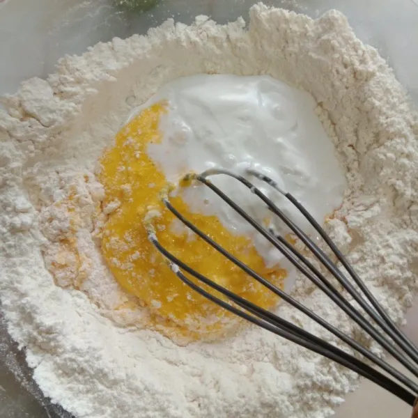 Siapkan wadah, ayak tepung terigu, beri lubang tengah di tepungnya, tuang kuning telur dan santan kental, aduk rata menggunakan ballonwhisk.