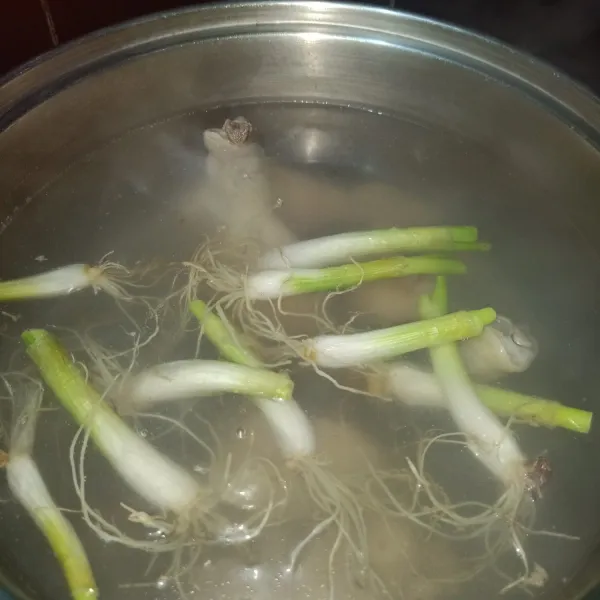 Masukkan akar bawang daun ke dalam panci berisikan rebusan ayam