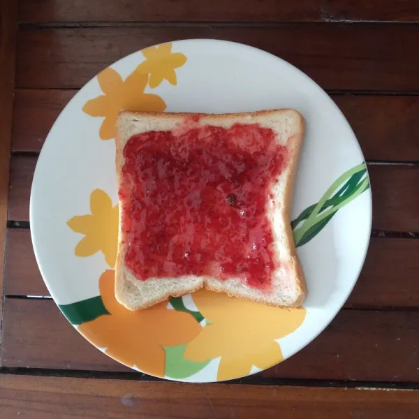 Ambil 1 lembar roti tawar, oleskan selai strawberry sampai merata.