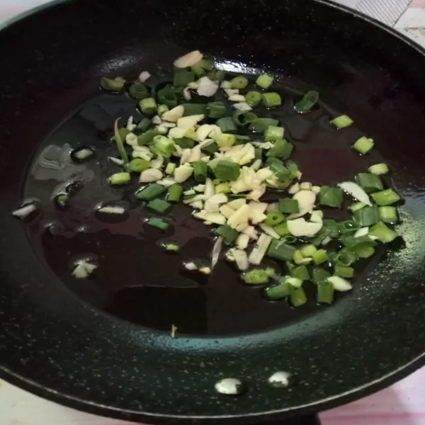 Panaskan teflon beri minyak, lalu tumis bawang putih dan daun bawang sampai layu.