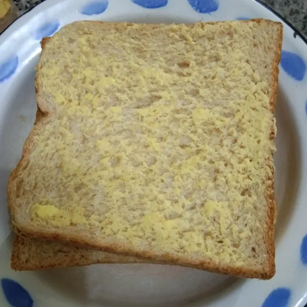 Olesi permukaan roti dengan margarin.