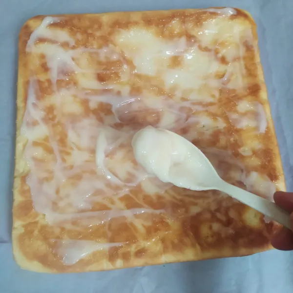 Tata di meja, serbet bersih dan kertas roti yang ukurannya lebih besar dari loyang. Lepaskan kertas alasnya tadi, lalu olesi dengan campuran mayonaise dan krimer kental manis. (Lakukan ketika roti masih panas supaya mudah menggulungnya)