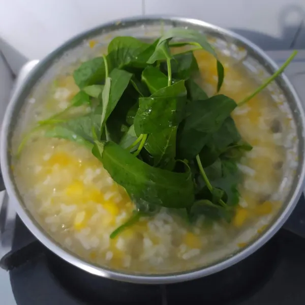 Masukkan sayuran ketika nasi sudah bertekstur bubur, aduk rata. Masak sampai sayuran layu. Kemudian bumbui dengan garam, koreksi rasa.