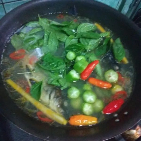 Masukan cabe rawit, kemangi, dan belimbing wuluh, lalu balik sisi ikan lainnya. Koreksi rasa sesuai selera lalu masak hingga ikan matang. Gunakan api kecil supaya kuah kaldu ikan lebih terasa.