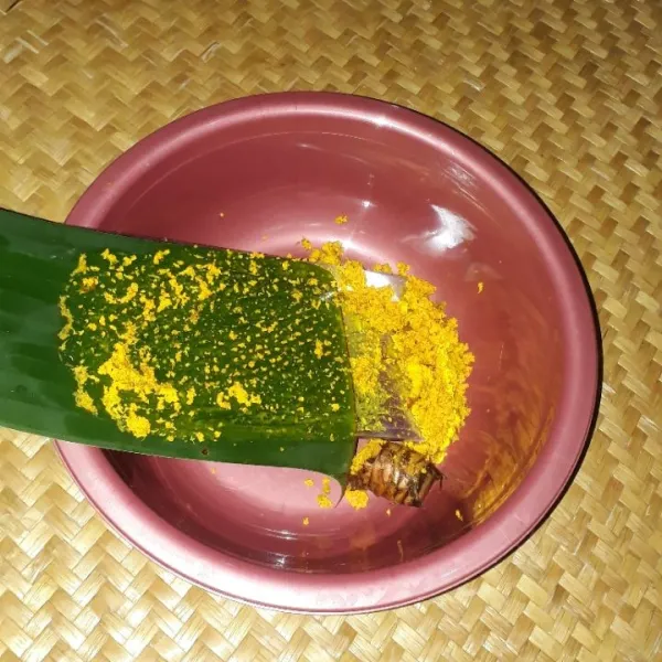 Parut kunyit dengan parutan yang telah di lapisi daun pisang agar getah kunyit tidak menempel pada parutan.