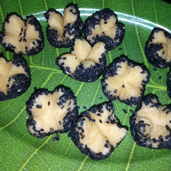 Gulingkan adonan ke dalam wijen hitam, kemudian pada bagian atas kue belah menjadi dua hingga berbentuk mekar.