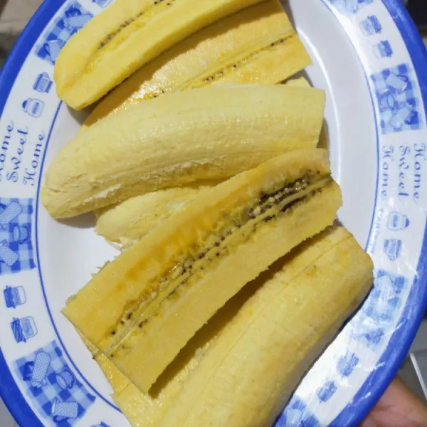 Kupas pisang, potong satu pisang, dibagi menjadi dua, dan belah menjadi empat bagian memanjang. Total 8 potong.