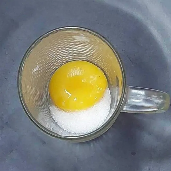 Masukkan gula pasir dan kuning telur ke dalam gelas