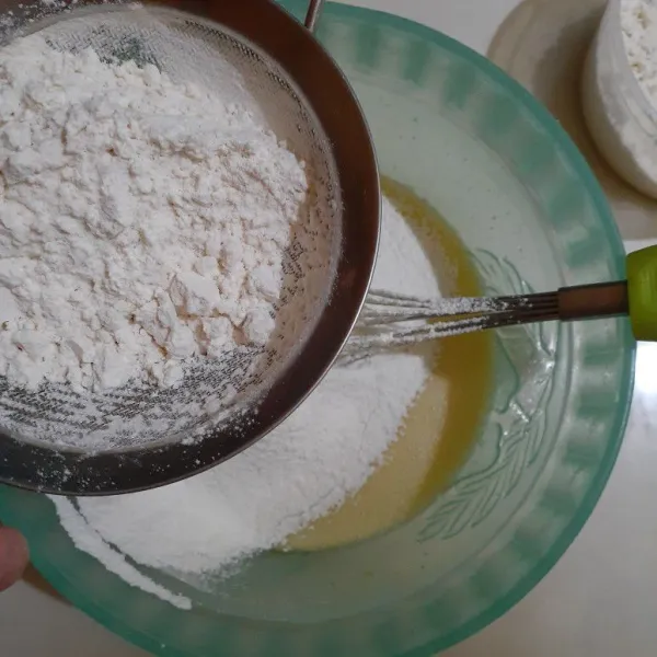 Masukkan sedikit demi sedikit campuran tepung, baking powder, baking soda, vanili bubuk sambil di saring. Aduk merata.