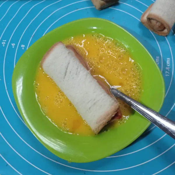Kocok telur dan susu cair, lalu celupkan di gulungan roti tawar.