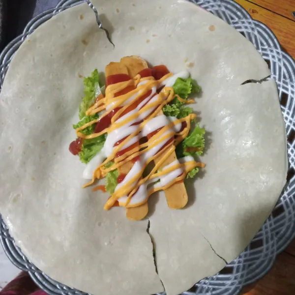Ambil selembar kulit tortila, beri 1/2 lembar keju slice, irisan selada, irisan mentimun, sosis, mayonaise, mayonaise pedas, saos tomat dan saos sambal. Timpa dengan 1/2 lembar keju slices, lalu lipat.