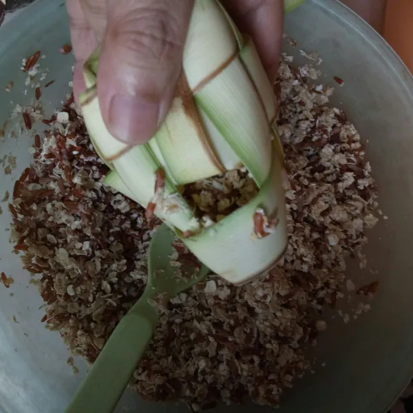 Masukkan beras oat ke dalam bungkus ketupat hingga setengah bagian.