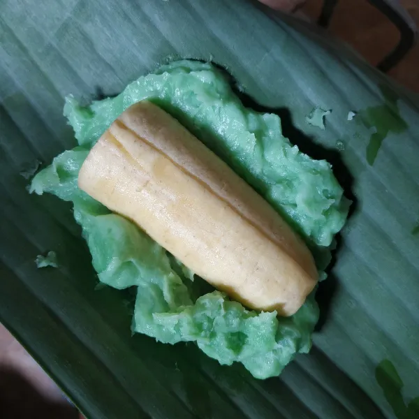 Ambil 1 lembar daun pisang, beri adonan tepung secukupnya tambahkan 1 potong pisang. Gulung kemudian lipat.