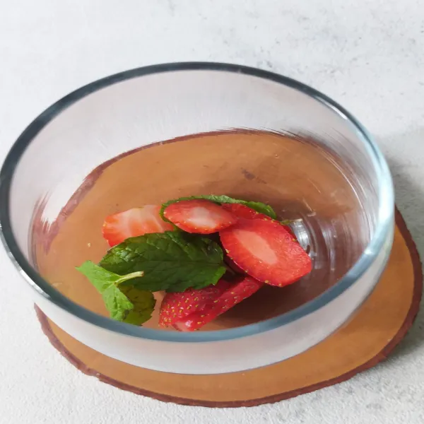 Tuang ke gelas irisan buah strawberry dan daun mint.