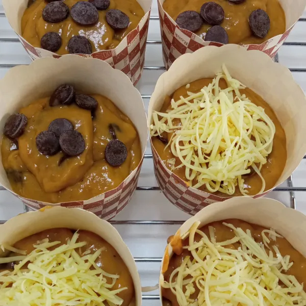 Tuang adonan dalam cup muffin, 1/2 adonan topping chocolate button, dan 1/2 adonan topping cheese.