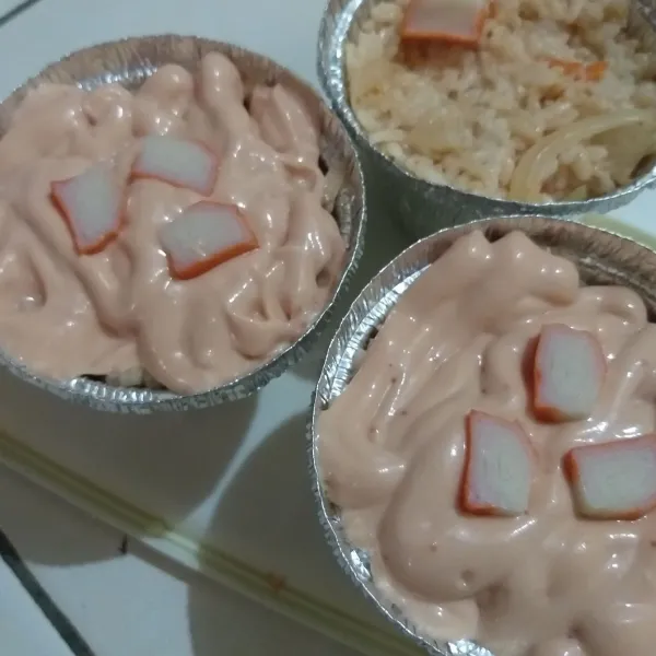 Siapkan wadah aluminium foil, masukkan nasi yang sudah dibumbui. Kemudian masukkan saus mentai ke dalam piping bag, dan tuang secara merata ke atas nasi, dan beri toping kani di atasnya.