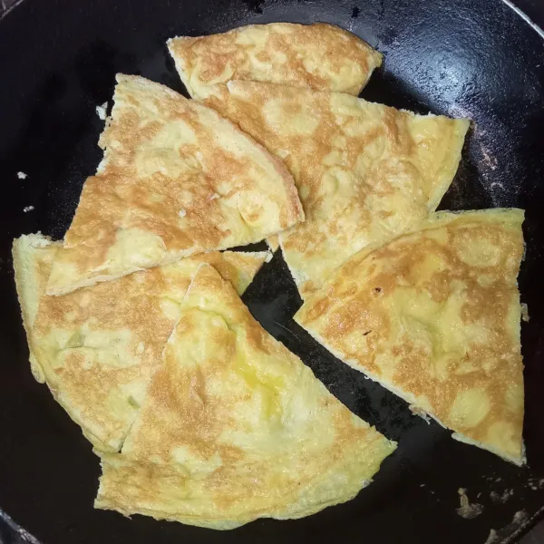 Potong-potong telur dadar jadi beberapa bagian.