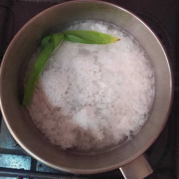 Membuat bubur : masak nasi, air, garam dan daun pandan sampai air meresap.