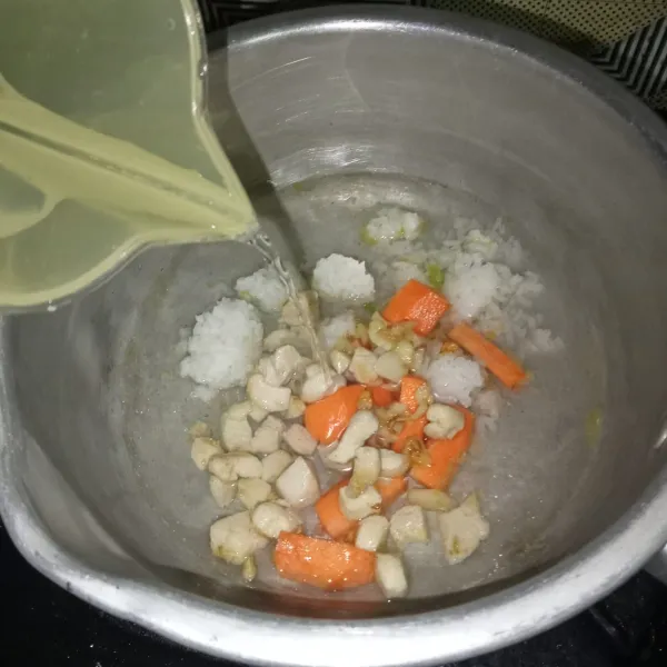 Masukkan nasi, wortel, air dan ayam yang sudah ditumis kedalam panci, lalu rebus hingga menjadi bubur.