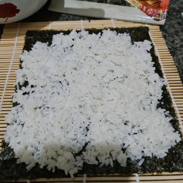 Bentangkan nori sheet pada sushi mat. Beri nasi dan ratakan.