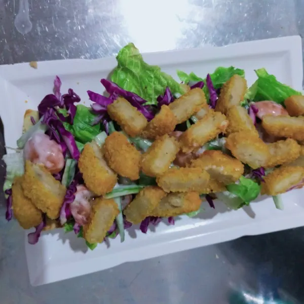 Ambil selembar roti, tata bahan salad di atasnya, beri irisan nugget, dan saus sambal. Tutup lagi dengan roti.