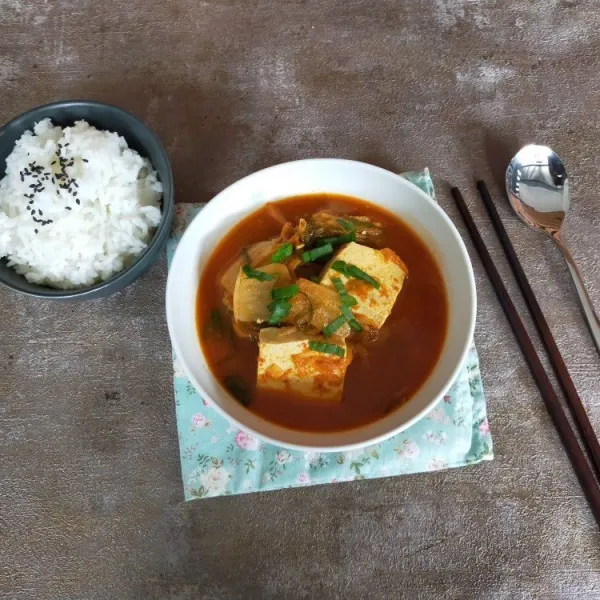 Sajikan sup kimchi dengan taburan daun bawang dan nasi hangat.