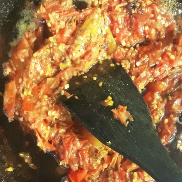 Panaskan minyak goreng di wajan dengan api sedang. Masukkan ulekan tomat dan cabai rawit, kemudian masak dan sesekali aduk rata agar tidak menempel dan gosong.