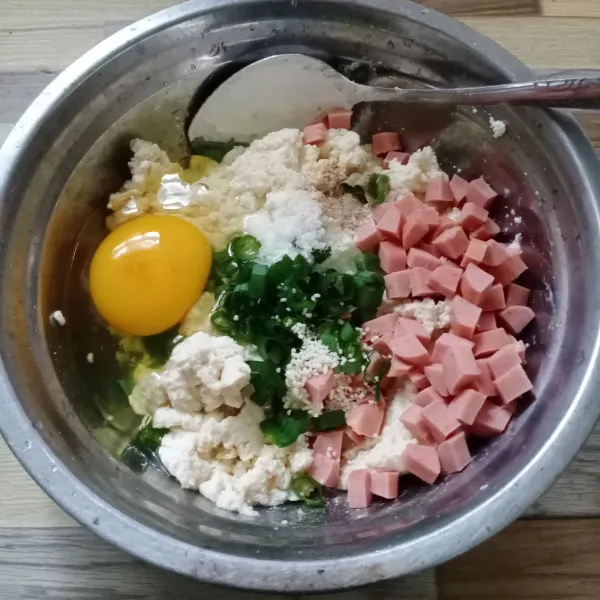 Masukkan tahu, telur, sosis, maizena, daun bawang, garam, kaldu jamur dan lada bubuk ke dalam wadah. Aduk sampai tercampur rata.