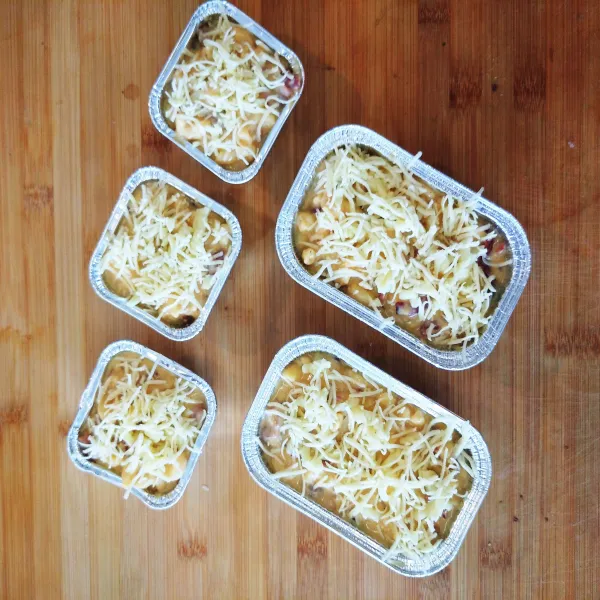 Siapkan wadah aluminium foil, tuang adonan macaroni schotel. Taburkan parutan keju mozzarella dan keju cheddar. Panggang selama 15 menit dalam oven dengan suhu 180°C.