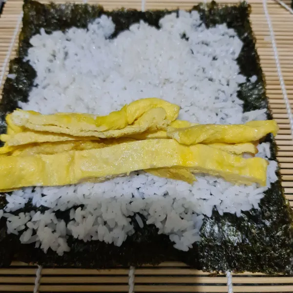 Bentangkan nori diatas sushi mat lalu beri nasi, ratakan dan tata telur dadar.