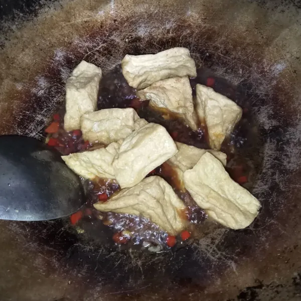 Masukkan air, kecap manis, garam, gula merah dan kaldu jamur, aduk hingga tercampur rata. Lalu masukkan tahu goreng.