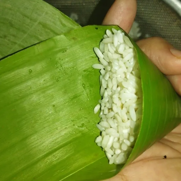Lalu bentuk kerucut daun pisangnya, lalu isi penuh dengan beras ketan, lalu lipat hingga beras ketan tertutup.