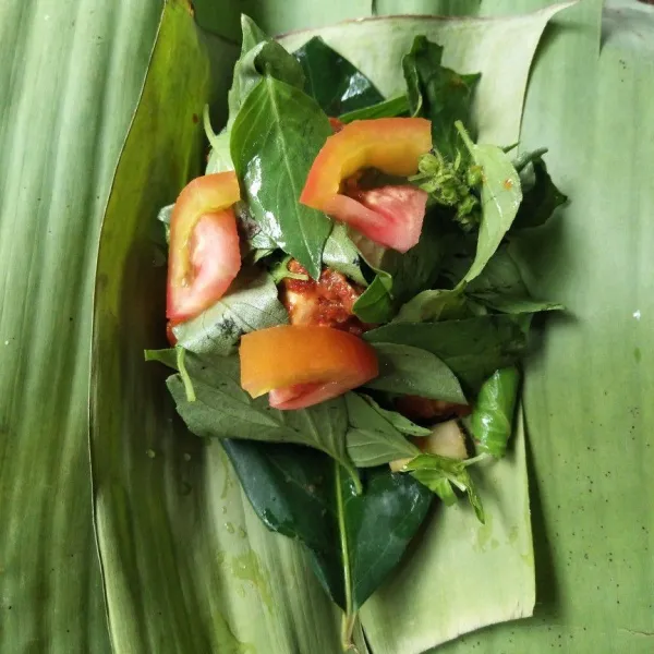 Siapkan daun pisang, kemudian masukkan daun salam, serai, ayam, tomat, dan kemangi. Lalu, gulung dan sematkan lidi.