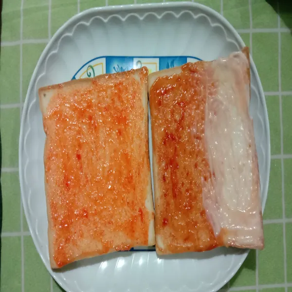 Oles merata saus sambal, saus tomat, dan mayonaise di atas roti sesuai selera.