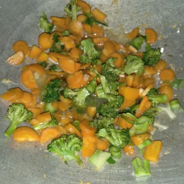Masukkan iridan brokoli dan wortel. Tambahkan 4 sdm air. Masak sayuran hingga setengah matang.