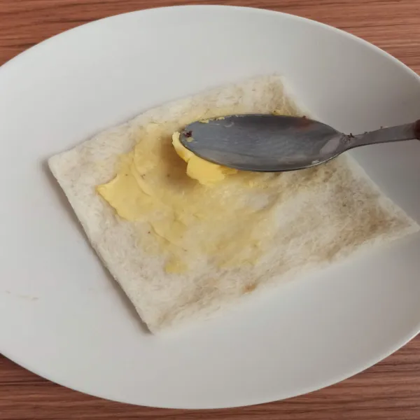 Ambil 1 lembar roti tawar, pipihkan kemudian olesi tipis dengan margarin.