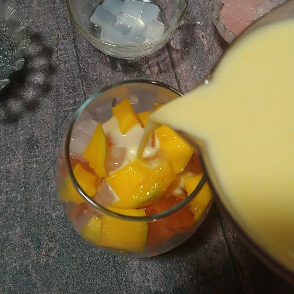 Ambil gelas, tuang sagu mutiara, jelly, nata de coco, dan irisan buah mangga. Lalu tuang saus creamynya.