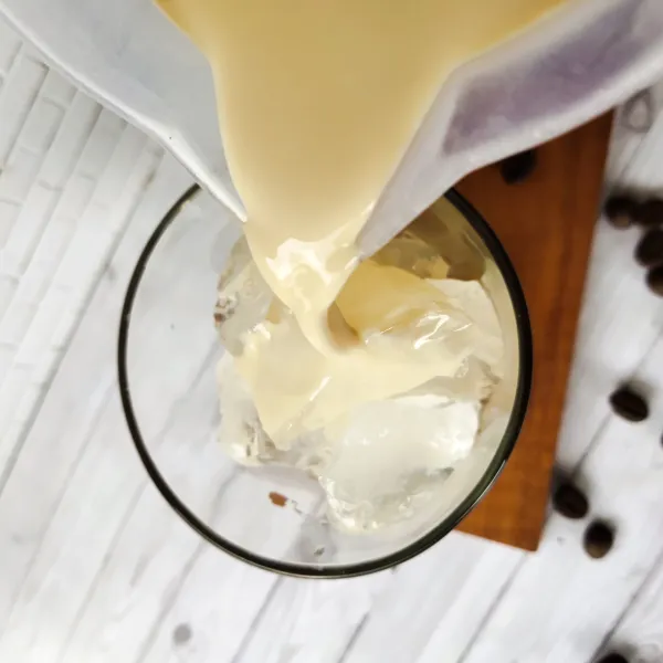 Tuang susu UHT rasa karamel pada gelas berisi es batu, aduk kembali.