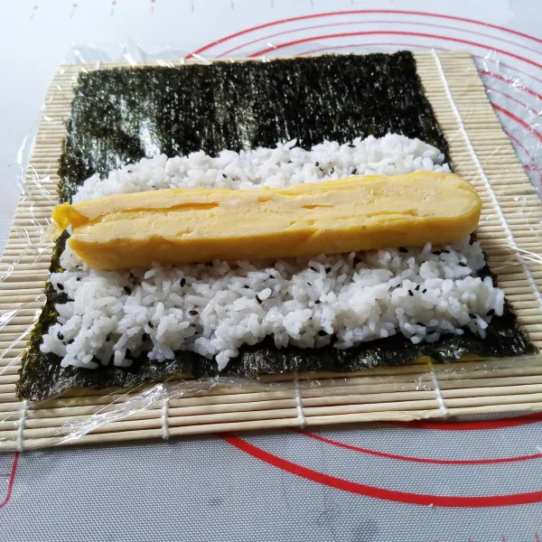 Bentangkan nori, ambil setengah bagian nasi sushi, ratakan, lefakkan potongan telur ditengah.