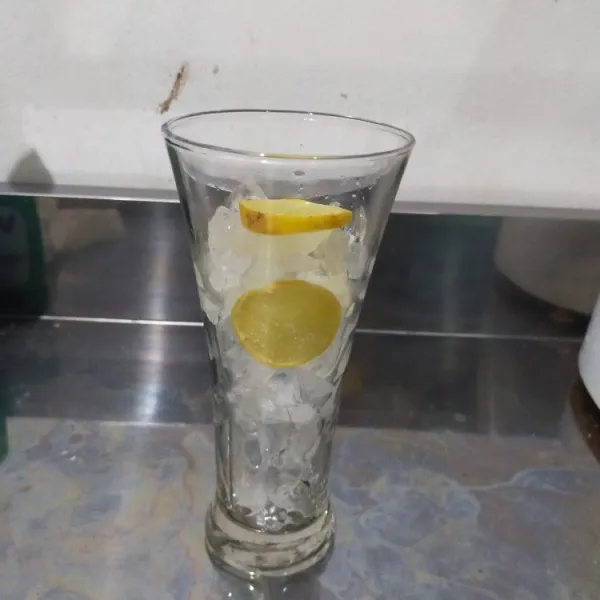 Siapkan gelas saji, beri es batu secukupnya dan irisan buah lemon.