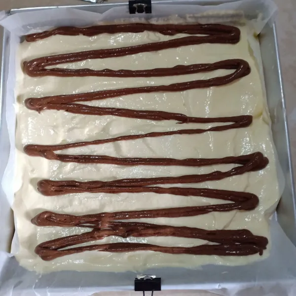 Ambil 1/3 adonan, lalu campurkan dengan cokelat bubuk, masukkan dalam piping bag. Isi loyang dengan adonan asal untuk sebagai alas saja, isi dengan adonan cokelat bergambar zig-zag.