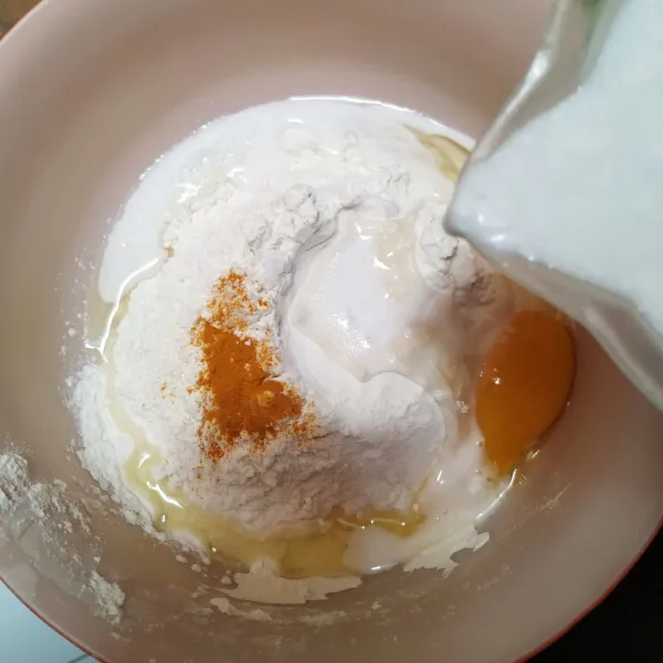 Dalam baskom, campur tepung terigu, gula pasir, telur, vanili, kunyit dan garam. Tuang santan sedikit demi sedikit sambil diaduk sampai tercampur rata.